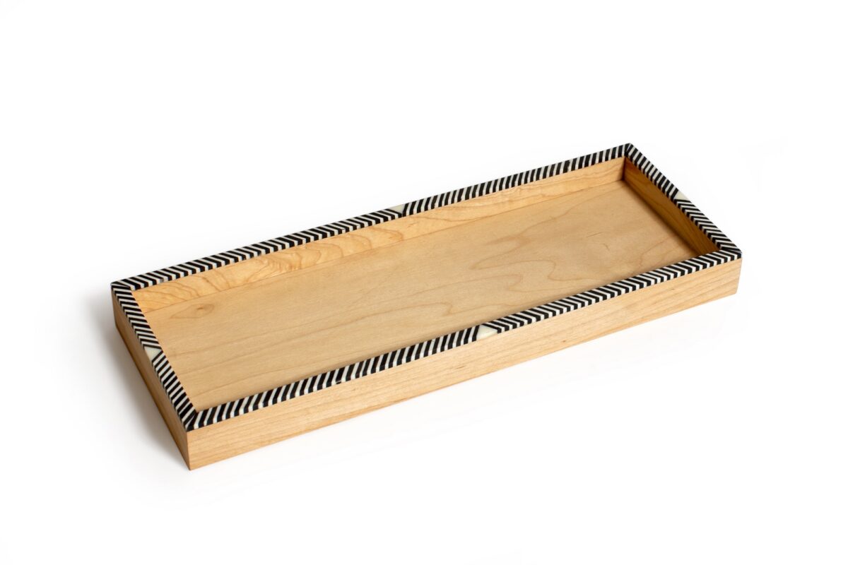 alt="wooden tray with camel bones, geometrical dotted black and white design on edges"