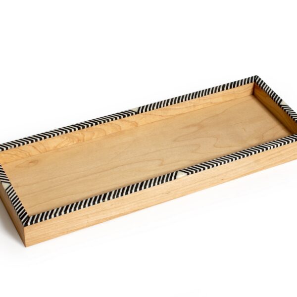 alt="wooden tray with camel bones, geometrical dotted black and white design on edges"